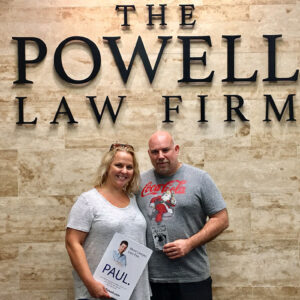 Couple standing in front of The Powell Law Firm sign, holding a promotional flyer and a gift card for personal injury legal services in Las Vegas.