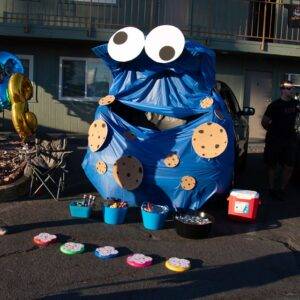 A car trunk decorated as a Cookie Monster for a community event in Las Vegas, with buckets of treats and a man standing nearby, possibly related to personal injury outreach.
