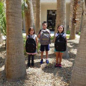 Three smiling children with backpacks stand among palm trees in Las Vegas, symbolizing the importance of child safety and the need for personal injury legal representation in case of accidents involving kids.
