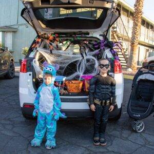 Two children dressed in costumes stand in front of a car decorated for a trunk or treat event with Halloween decorations, representing family fun and community safety in Las Vegas.