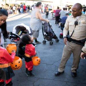 A diverse crowd, including children in Halloween costumes, gather at a community event in Las Vegas with law enforcement present to ensure safety.