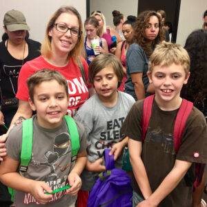 A group of smiling children and adults pose for a photo with backpacks at a community support event in Las Vegas, possibly related to personal injury assistance.