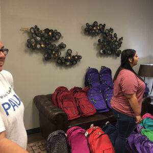 A Las Vegas personal injury law firm hosts a backpack drive for the local community, with colorful backpacks stacked on furniture and people smiling.