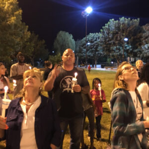 A group of diverse individuals in Las Vegas hold candles during a nighttime vigil to remember personal injury victims, showing support and solidarity.