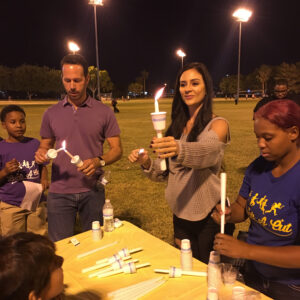 A group of people at night, standing around a table and lighting candles for a vigil, possibly related to a personal injury case in Las Vegas.