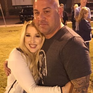 A friendly, smiling woman with blonde hair embraces a man with tattoos, conveying a sense of caring and support that a personal injury law firm in Las Vegas would offer to their clients.