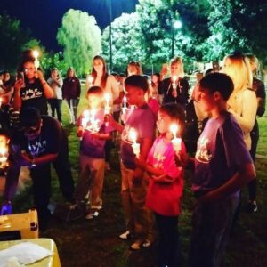 A nighttime outdoor vigil with diverse adults and children holding candles, likely a memorial or awareness event in Las Vegas relating to personal injury, loss, and community support.