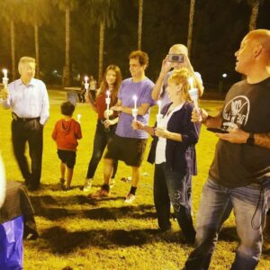 Group of people holding candles in a park at night, possibly a vigil or community event, symbolizing care and support for personal injury victims.