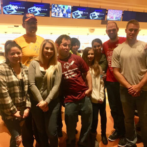 A group of diverse individuals, likely representing a Las Vegas-based personal injury law firm, poses for a group photo at a bowling alley, suggesting a team-building or social event, emphasizing community involvement and a friendly atmosphere within the firm.