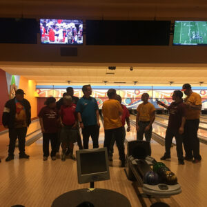 Lawyers and staff from a Las Vegas personal injury law firm at a bowling event, promoting team building and community involvement, with football games on in the background.