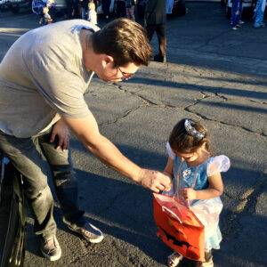 Image of a father giving a little girl dressed as a princess candy during a Halloween event in Las Vegas, conveying a message of protecting families and children from potential injuries.