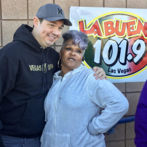 A Las Vegas Personal Injury attorney poses with a community member in front of the "La Buena 101.9 Las Vegas" radio station banner, symbolizing local support and community engagement.