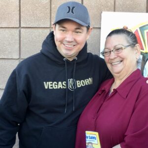 Smiling lawyer wearing a "Vegas Born" hoodie stands with a community member holding a safety booklet, representing commitment to Las Vegas residents and personal injury advocacy.
