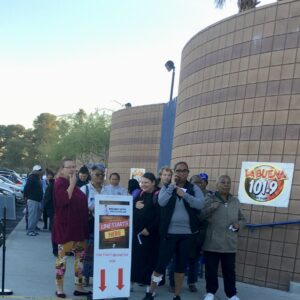 A diverse group of people line up in Las Vegas, some possibly injured, at an event with a sign promoting a personal injury law firm and radio station, suggesting community outreach and potential legal assistance after accidents.