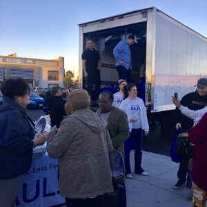Image shows volunteers from a Las Vegas law firm, likely specializing in personal injury, participating in a community outreach event involving a truck and distribution of goods.