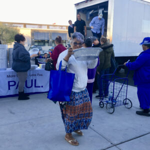 Image shows a community event by a Las Vegas law firm, possibly related to personal injury, with volunteers distributing items to people lined up, and a sign that reads "More L : Less Fee."
