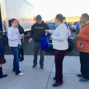 Volunteers and staff from a Las Vegas personal injury law firm distribute materials and bags to community members outdoors near a truck, showcasing their commitment to supporting the local community.