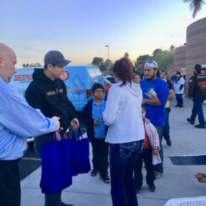 A group of people gather outside in Las Vegas, some receiving blue tote bags, potentially as part of a community outreach event supported by a personal injury law firm.