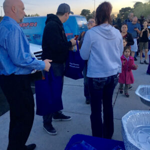 A community event hosted by a Las Vegas law firm shows people receiving blue tote bags in front of a branded van with a crowd of families nearby, highlighting community involvement and support for personal injury victims.