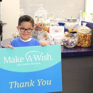 A young boy stands in front of a candy bar with a Make-A-Wish Southern Nevada "Thank You" sign, showcasing the law firm's community involvement and charitable support in Las Vegas.