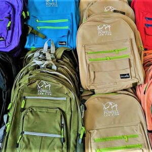 Close-up shot of colorful backpacks with the logo of The Powell Law Firm, a Las Vegas Personal Injury law firm, displayed prominently on each one.