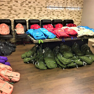 A large collection of backpacks in various colors with the Powell Law Firm logo, a Las Vegas personal injury law firm, displayed on chairs and a table, suggesting a community outreach or giveaway event.