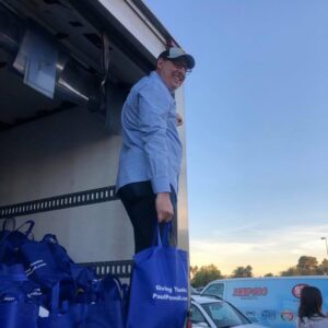 Image of a Las Vegas attorney from a personal injury law firm standing in the back of a truck filled with "Giving Thanks PaulPowell.com" blue bags, likely for a community event, showing the firm's commitment to serving and supporting the local community.