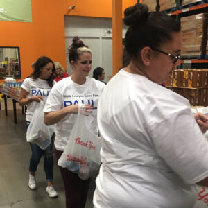 The image features team members from a Las Vegas law firm, possibly specializing in personal injury, volunteering and distributing items in a warehouse setting.