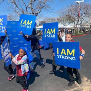 A group of children walks in a Las Vegas charity event, holding signs saying "I AM LIMITLESS," "I AM A STAR," and "I AM STRONG" representing the resilience and hope needed after a personal injury.