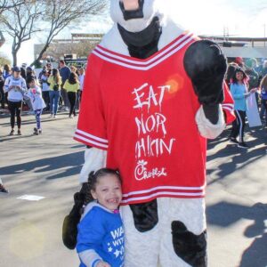 A happy child stands with the Chick-fil-A mascot, highlighting the importance of protecting loved ones with a qualified personal injury attorney in Las Vegas after an accident.