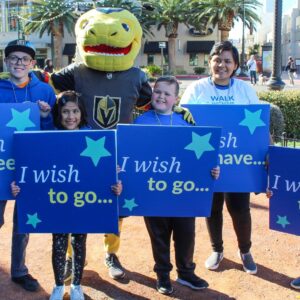 A group of children and an adult hold signs reading "I wish to..." while posing with a Golden Knights mascot outdoors, representing support for children's wishes in Las Vegas, which can be relevant to personal injury cases involving children.