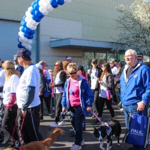 A diverse crowd walks with dogs under a balloon arch, symbolizing community support and injury prevention awareness, relevant to a personal injury law firm in Las Vegas.