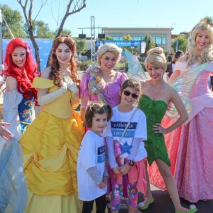 A vibrant outdoor event hosted by a Las Vegas Personal Injury Law Firm featuring Disney princesses, fairies, and children wearing firm t-shirts, symbolizing community engagement and family-friendly legal support.