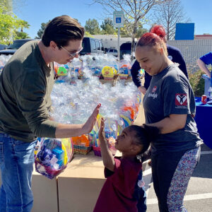 Image of a personal injury law firm in Las Vegas participating in a community event, with a lawyer giving a high-five to a child amidst a backdrop of Easter baskets, promoting a caring and supportive image.