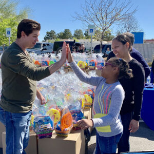 Image of a personal injury law firm in Las Vegas engaging with the community at an event, showing a man giving a high-five to a child surrounded by gift baskets, symbolizing support and care for individuals, especially children, reflecting the firm's commitment to community welfare.