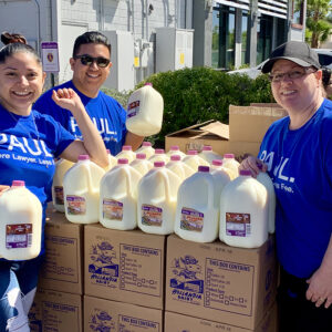Group of smiling individuals in blue "PAUL More Lawyer Less Fee" shirts are distributing gallons of Hollandia Dairy milk in Las Vegas, showcasing community involvement and support for personal injury clients.