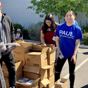 Smiling volunteers pack boxes of food items, including dried figs and canned goods, for a community service event hosted by a Las Vegas personal injury law firm, emphasizing their commitment to helping those in need.