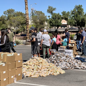 A Las Vegas community food distribution event with volunteers and residents gathering around boxes of food and supplies on a sunny day, reflecting the firm's commitment to the well-being of the community they serve.