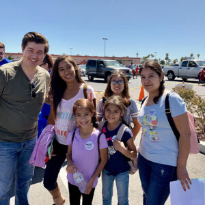 A group of adults and children gather outside at a community event in Las Vegas, possibly related to personal injury awareness, with cars and buildings visible in the background.