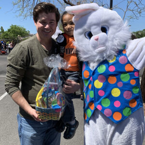 A Las Vegas personal injury attorney poses with a child holding an Easter basket and the Easter Bunny at a community event, showcasing the firm's commitment to family and safety.