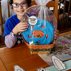 Smiling child with bunny ears holding an Easter basket with a sticker for "More Lawyer, Less Fee" from a personal injury law firm in Las Vegas, promoting safety awareness during the holiday season.