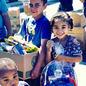 A group of smiling children carrying food and gift baskets, emphasizing the Las Vegas personal injury law firm's commitment to the community and its care for the well-being of local families.