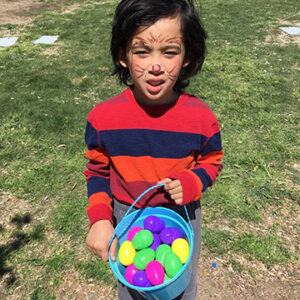 A young boy with face paint holds a bucket of colorful Easter eggs, symbolizing the preciousness of family and the need for personal injury protection.