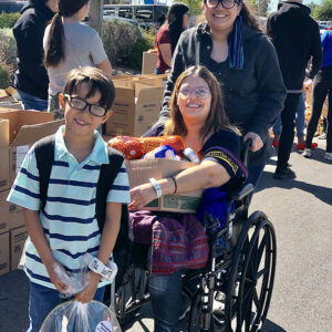 A group of smiling individuals, including a person in a wheelchair, participate in a charitable event, possibly related to personal injury support in Las Vegas, with boxed goods and gift baskets visible, suggesting a community outreach program.