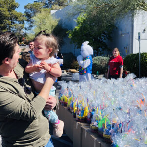 Las Vegas attorney holds a child near a large display of Easter baskets, with the Easter bunny and a volunteer in the background at a community event, promoting safety and community support after personal injuries.