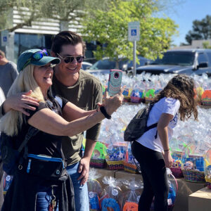 Image shows a woman taking a selfie with a man in front of tables filled with Easter baskets at a community event, possibly sponsored by a law firm, in Las Vegas, highlighting community involvement and support for families, despite any personal injury issues they may face.