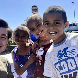 A Las Vegas personal injury lawyer smiles with children wearing "More Lawyer, Less Fee" buttons at a community event.