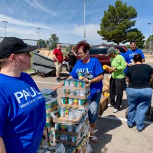 Volunteers wearing "Paul: More Lawyer. Less Fee" shirts stack and distribute canned goods at an outdoor Las Vegas food drive, showcasing community involvement by the personal injury law firm.