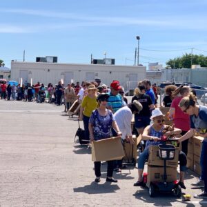A long line of diverse people in Las Vegas, some with mobility issues and carts, wait in an outdoor parking lot, highlighting potential personal injury risks in community events.