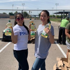 Two women holding vegetable oil bottles at a community food drive event, likely organized by a personal injury law firm in Las Vegas.